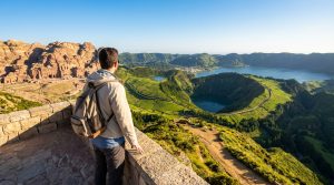 Un voyageur dos à la caméra contemple un panorama composite : les tombeaux de Pétra à gauche et les lacs volcaniques des Açores à droite.