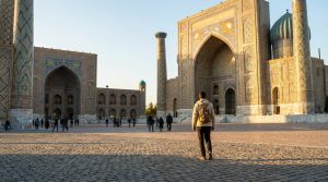 Voyageur solo avec sac à dos marchant sur la Place du Registan à Samarkand. Architecture islamique grandiose au soleil couchant.
