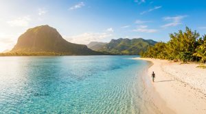 Plage paradisiaque à l'île Maurice. Homme marchant sur le sable fin bordé d'une mer turquoise et de montagnes luxuriantes dont Le Morne.
