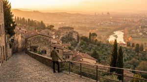 Un homme sur une rue pavée admire une vue panoramique sur une vallée, un fleuve et la ville de Florence au coucher du soleil.
